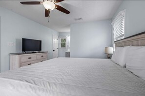 Un dormitorio con cama, televisor en una cómoda, ventilador de techo y ventana con persianas.