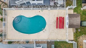 Una piscina rectangular con borde curvo, rodeada por una terraza y una valla blancos.