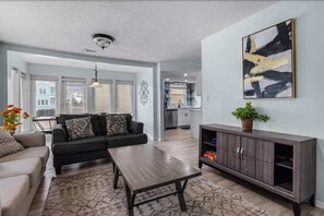 A modern living room with a sofa, coffee table, and a cabinet. There is a kitchen in the background with a sink and cabinets. - Sunny Coastal Cottage Near the Beach (North Myrtle Beach)