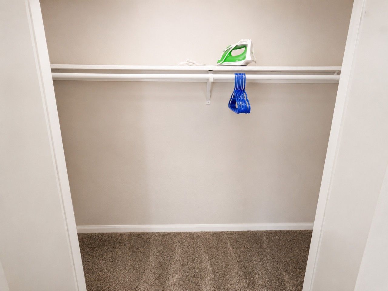 Ein Kleiderschrank mit Kleiderstange, einem blauen Gegenstand und einem Bügeleisen auf dem Regal.