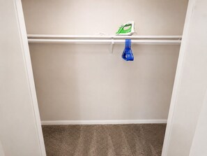 A closet with a hanging rod, a blue item, and an iron on the shelf.
