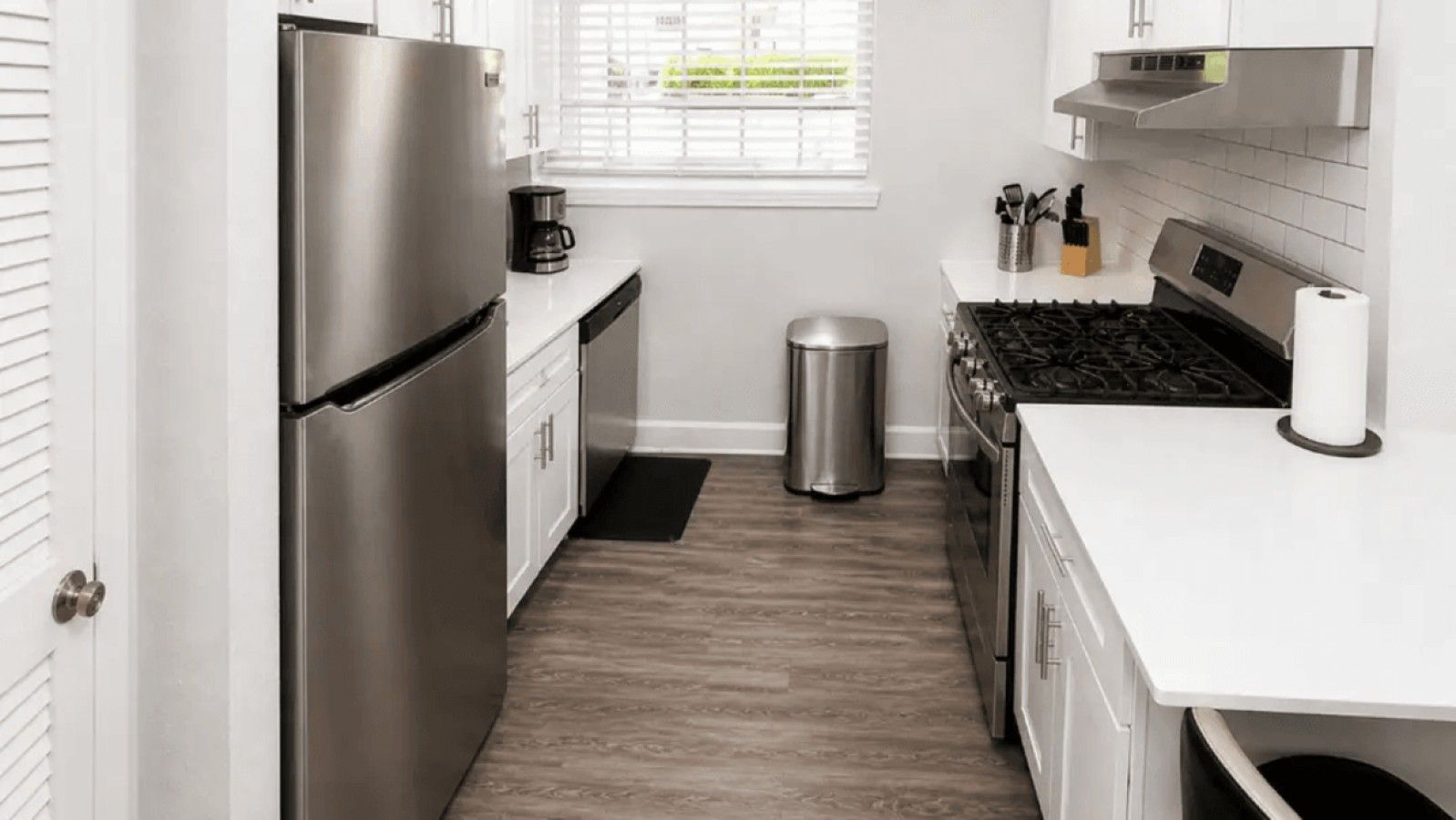 A compact kitchen with a stainless steel refrigerator, a stove, and a trash can.