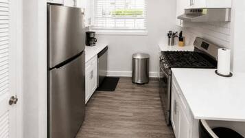A compact kitchen with a stainless steel refrigerator, a stove, and a trash can.