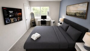 A bedroom with a bed, a desk, a computer, a TV, and a painting on the wall. - The Sutton | Modern 2BR Escape C2 (Hoover)