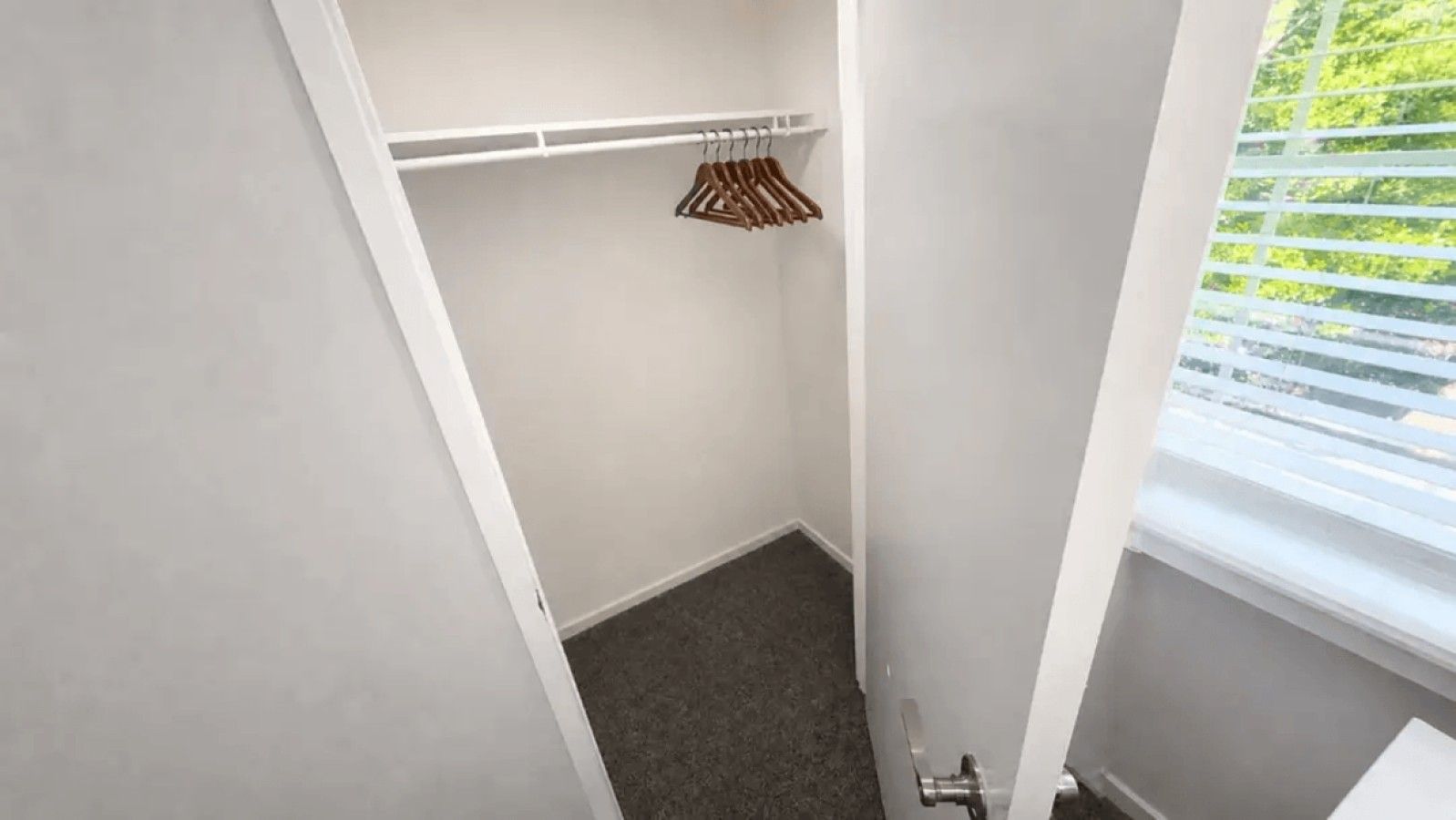 A small walk-in closet with a hanging rod and a window with blinds.
