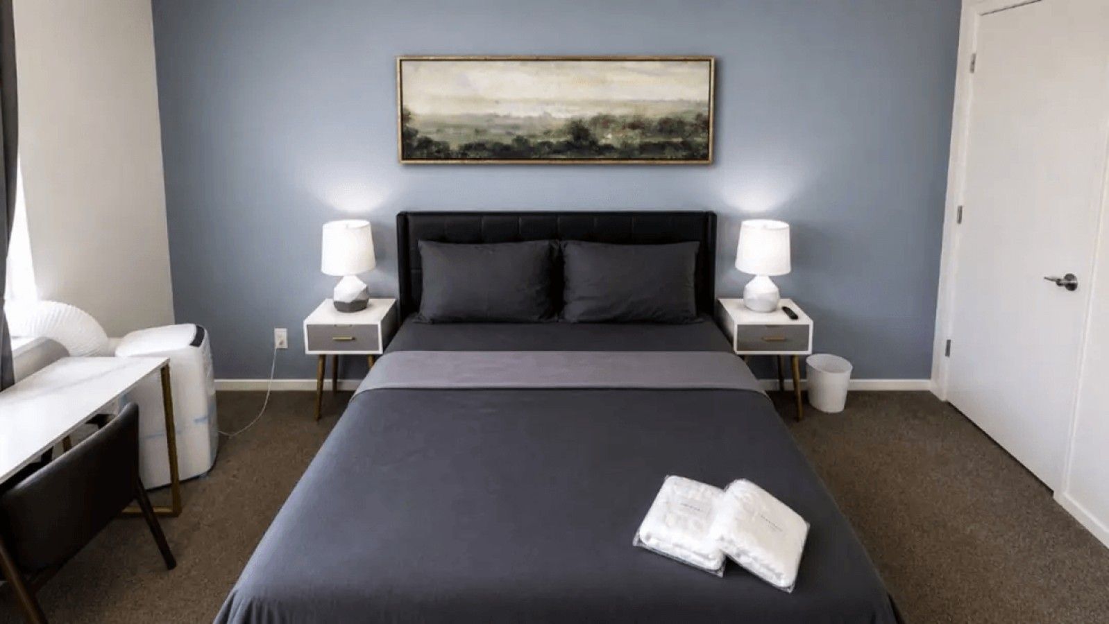 A hotel room with a large bed, bedside tables with lamps, a desk, and a chair.