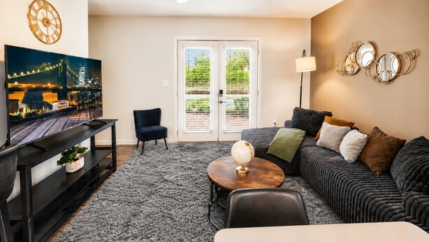 A living room with a television, a sofa, a coffee table, a chair, and a lamp. - The Sutton | Modern 2BR Escape C2 (Hoover)