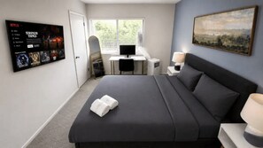 Ein Hotelzimmer mit einem Bett, einem Schreibtisch mit Computer, einem an der Wand montierten Fernseher und einem Bild an der Wand.