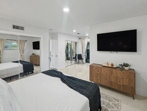 Une chambre d’hôtel moderne dotée d’un grand lit, d’un téléviseur à écran plat, d’une commode en bois et d’une porte-fenêtre coulissante donnant sur un balcon.