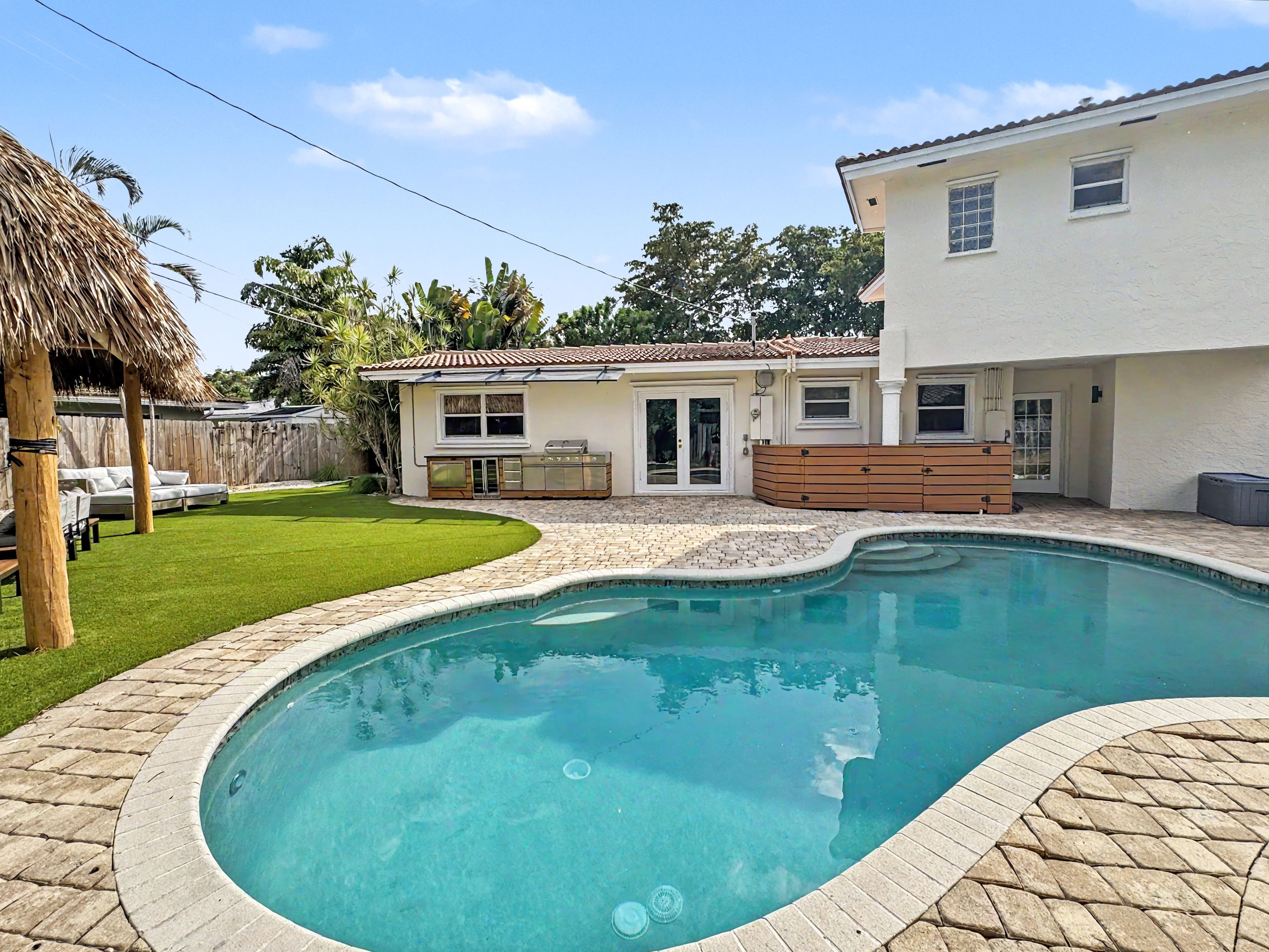 Um quintal com piscina, área de lazer e uma casa com telhado de azulejos e cerca de madeira.
