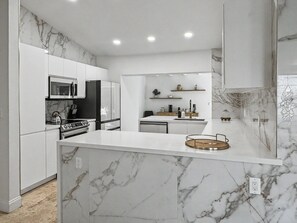 Une cuisine moderne avec des meubles blancs, un pare-feu en marbre et un îlot central.