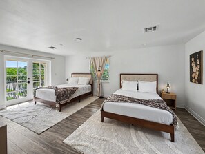 A bedroom with two beds, a large window, and a view of greenery. - Ultimate Group Getaway – Pool, Games & Tiki Bar (Wilton Manors)