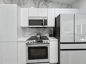 A modern kitchen with white cabinetry, a built-in microwave, a stainless steel stove, and a refrigerator. - Ultimate Group Getaway – Pool, Games & Tiki Bar (Wilton Manors)