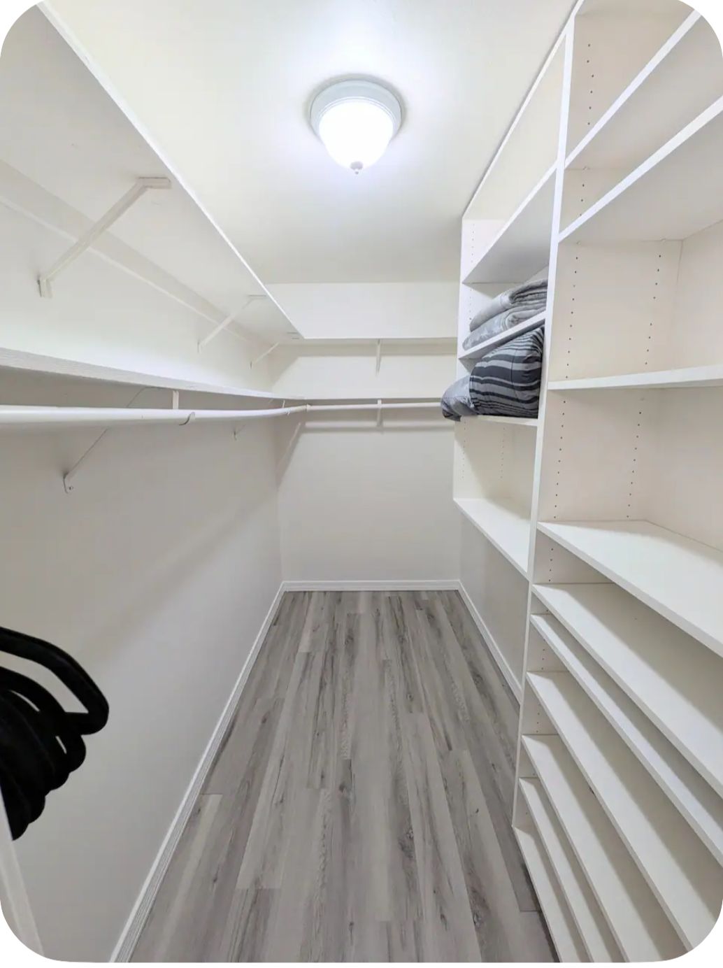 Un vestidor con estantes blancos, piso de madera gris y una luz en el techo.