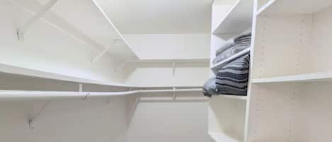 Un vestidor con estantes blancos, piso de madera gris y una luz en el techo.