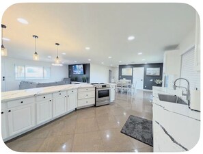 A modern kitchen with white cabinetry, a central island, and a dining area with a table and chairs. - Entertainment Home w/Game Room & Boat Parking! (Lake Havasu City)