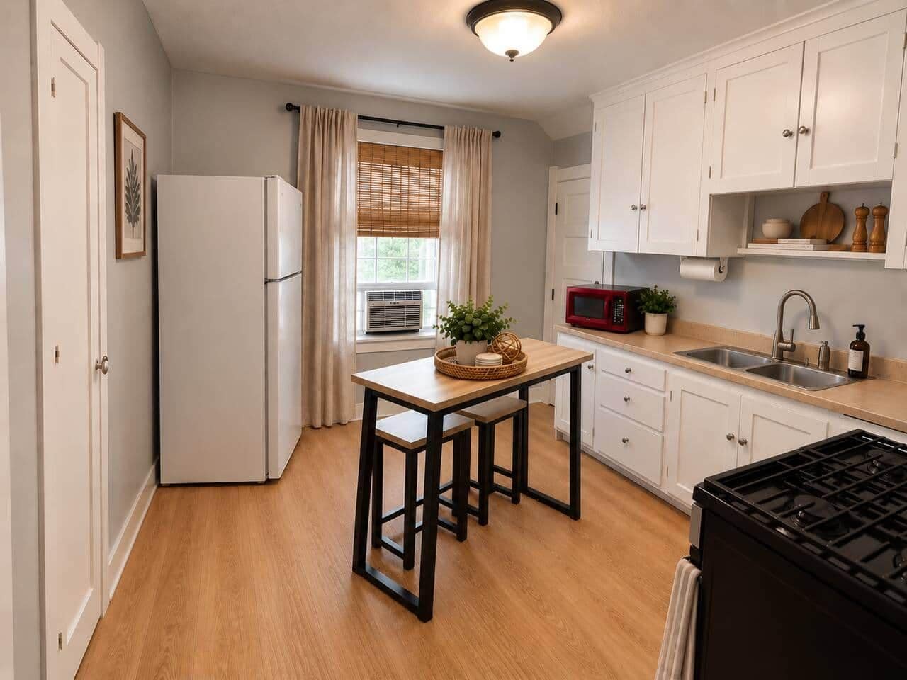 Una cocina pequeña con refrigerador, mesa y sillas, estufa y gabinetes blancos.