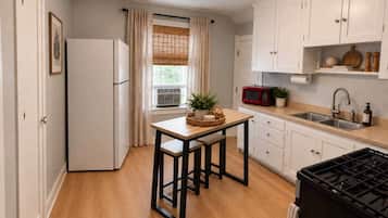 A compact kitchen with a refrigerator, a table with chairs, a stove, and white cabinets.