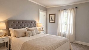 Een slaapkamer met een groot bed, een nachtkastje, een lamp en een ingelijst schilderij aan de muur.