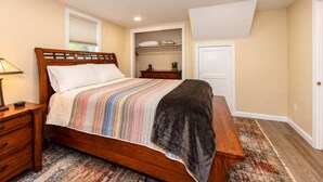A bedroom with a wooden bed, a bedside table, a nightstand, a bench, a window with blinds, a closet, and a door. - Cheyenne Plains 2 bedroom (Cheyenne)