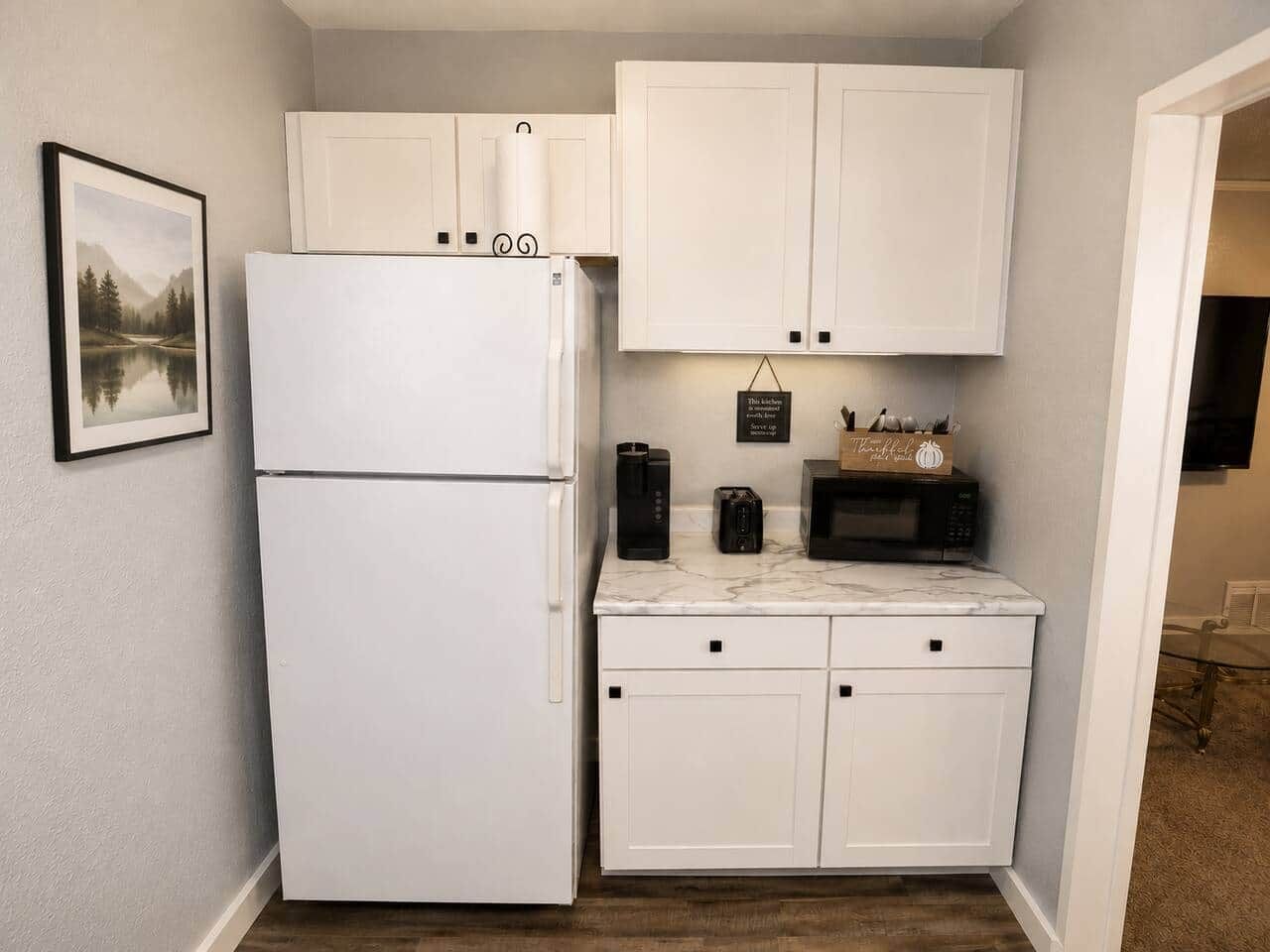 A compact kitchen with white cabinetry, a refrigerator, a microwave, and a coffee maker.
