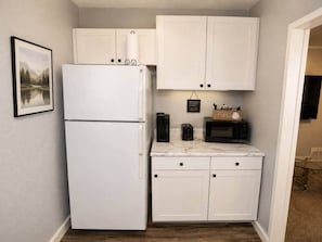 Una cocina compacta con muebles blancos, un refrigerador, un microondas y una cafetera.