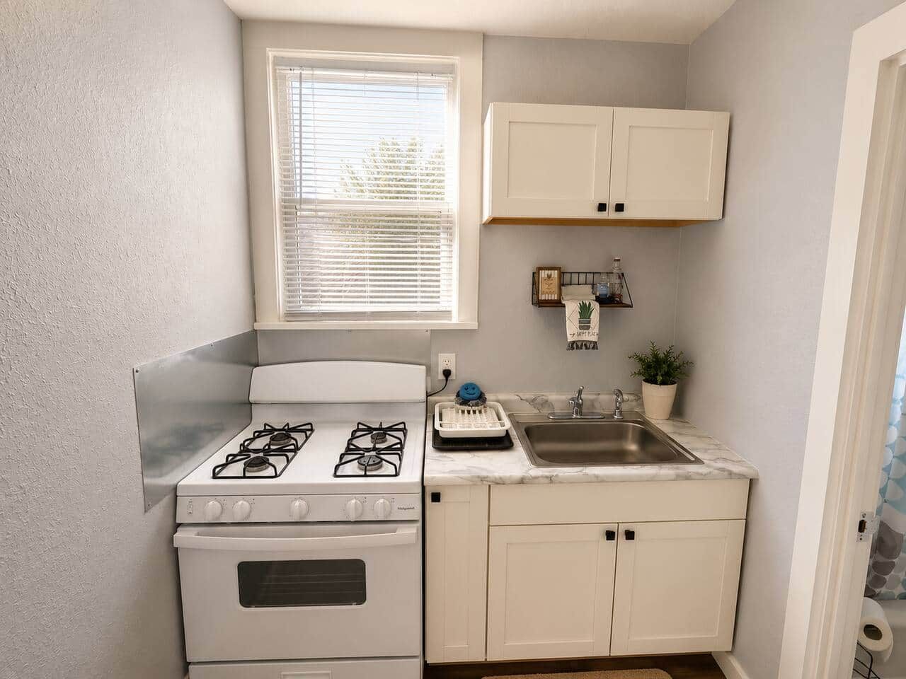 A compact kitchen with a gas stove, oven, sink, and white cabinetry.