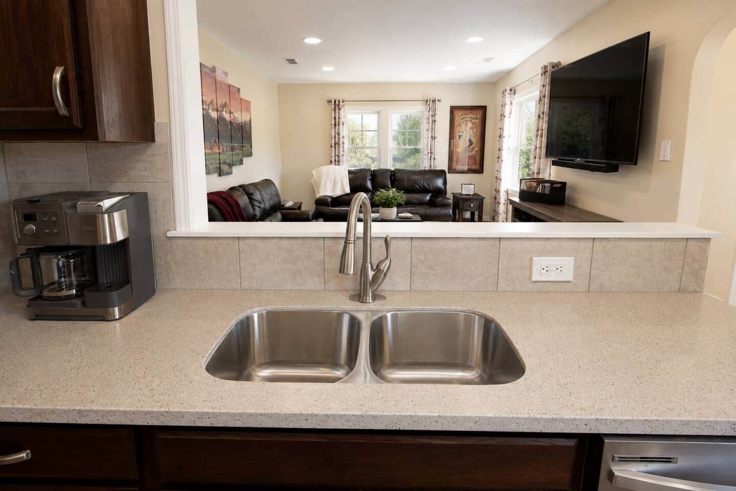 A kitchen with a double sink, a coffee maker, and a flat-screen TV mounted above the counter.