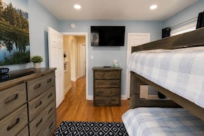 Quarto com cama beliche, penteadeira com gavetas, televisão na parede e relógio.