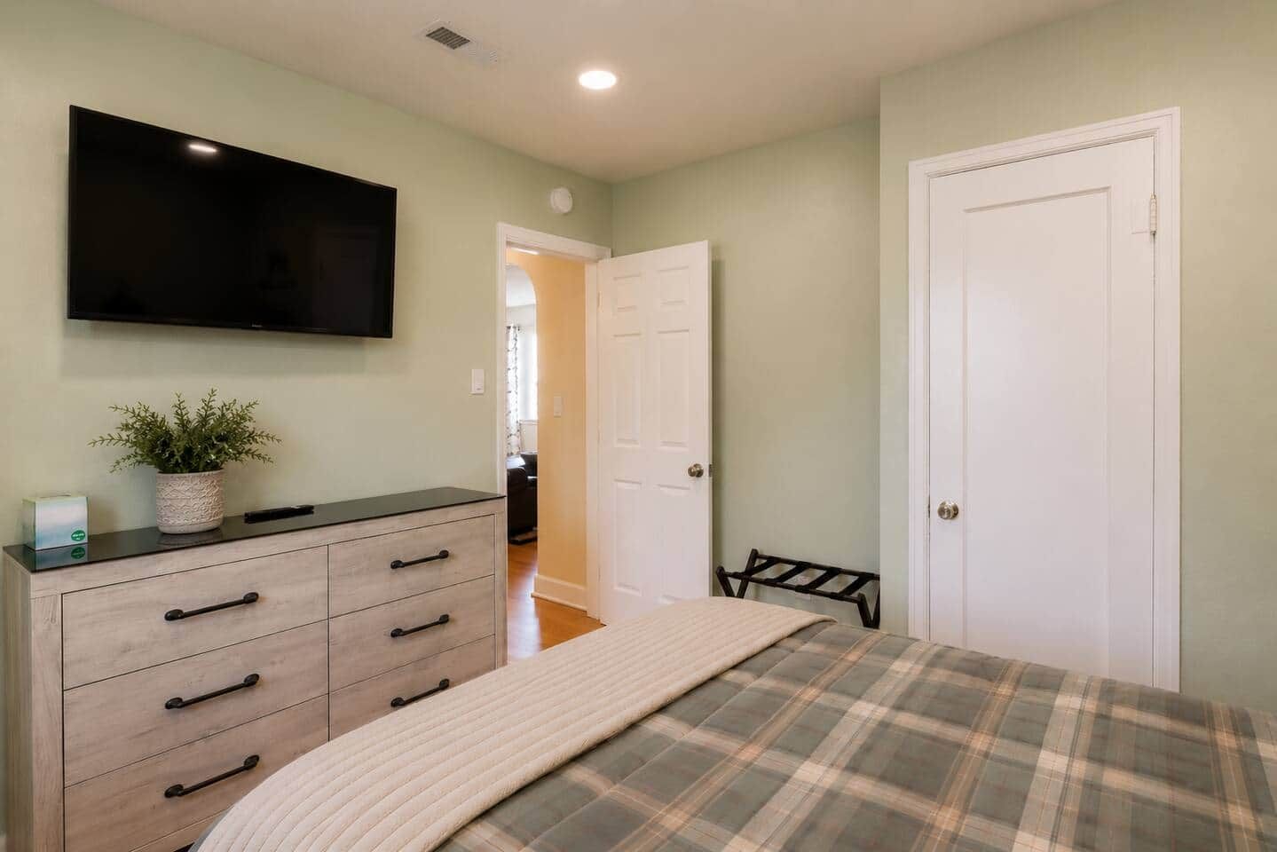 A bedroom with a bed, a dresser, a television, and a door.