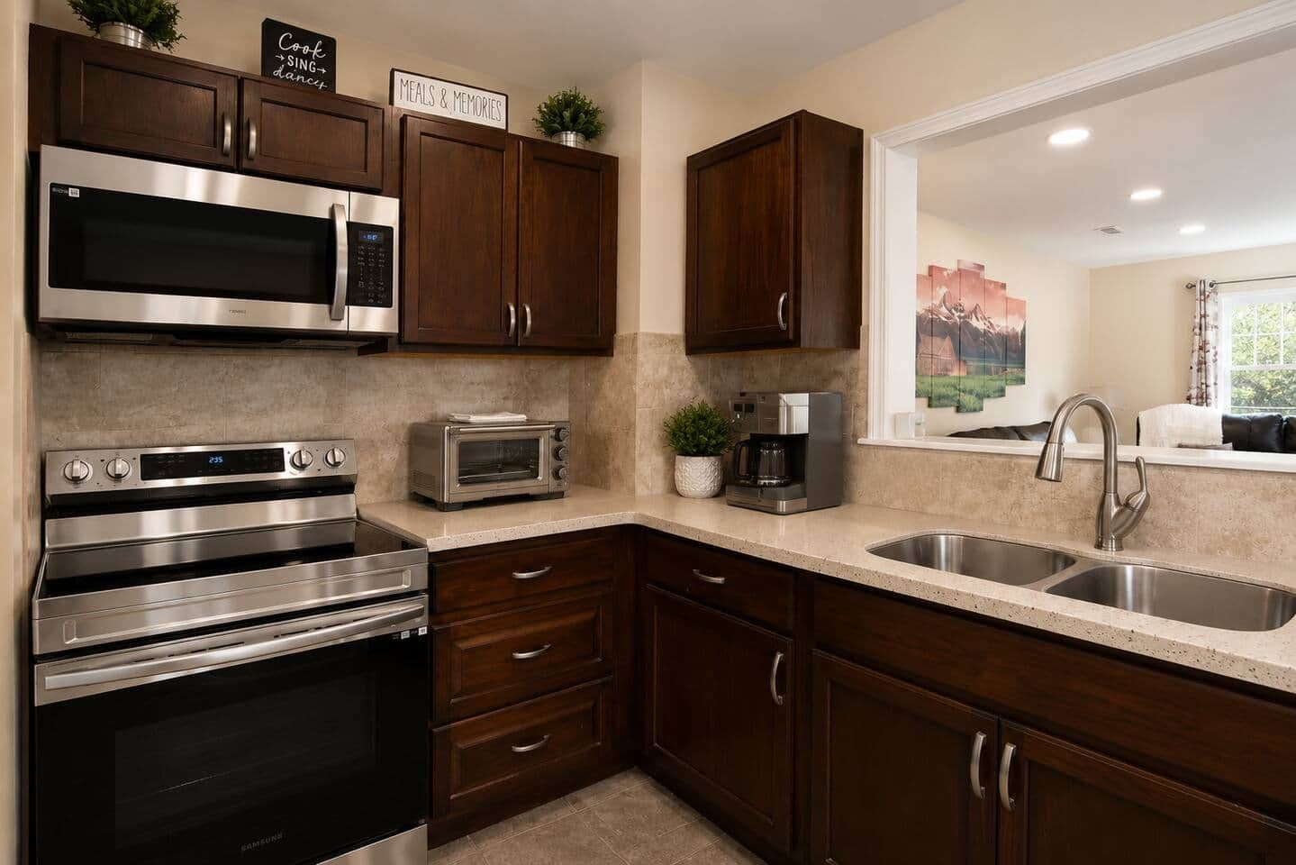 A modern kitchen with stainless steel appliances, dark wooden cabinets, and a large window.