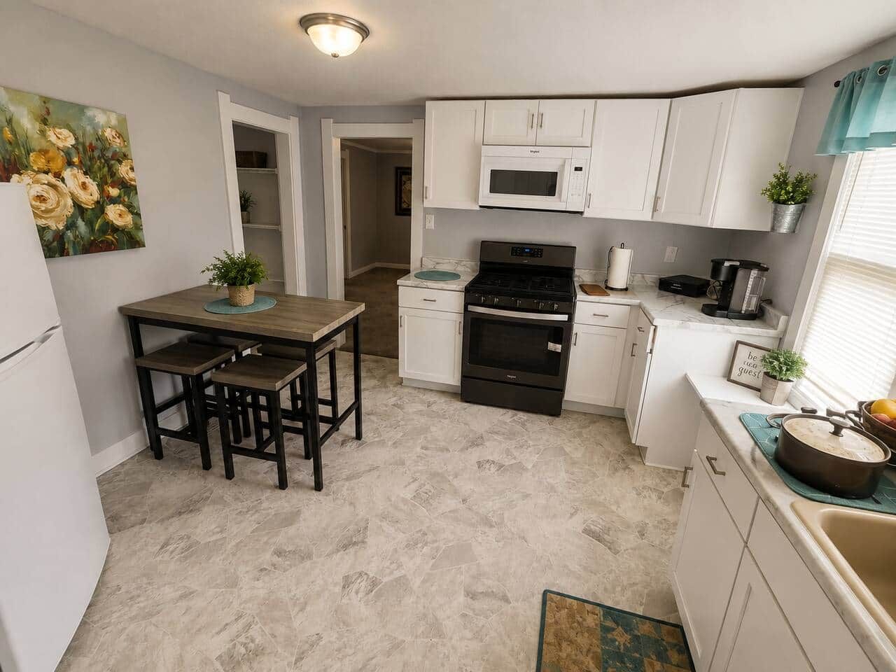 Una cocina compacta con armarios blancos, microondas, estufa y una mesa con bancos.