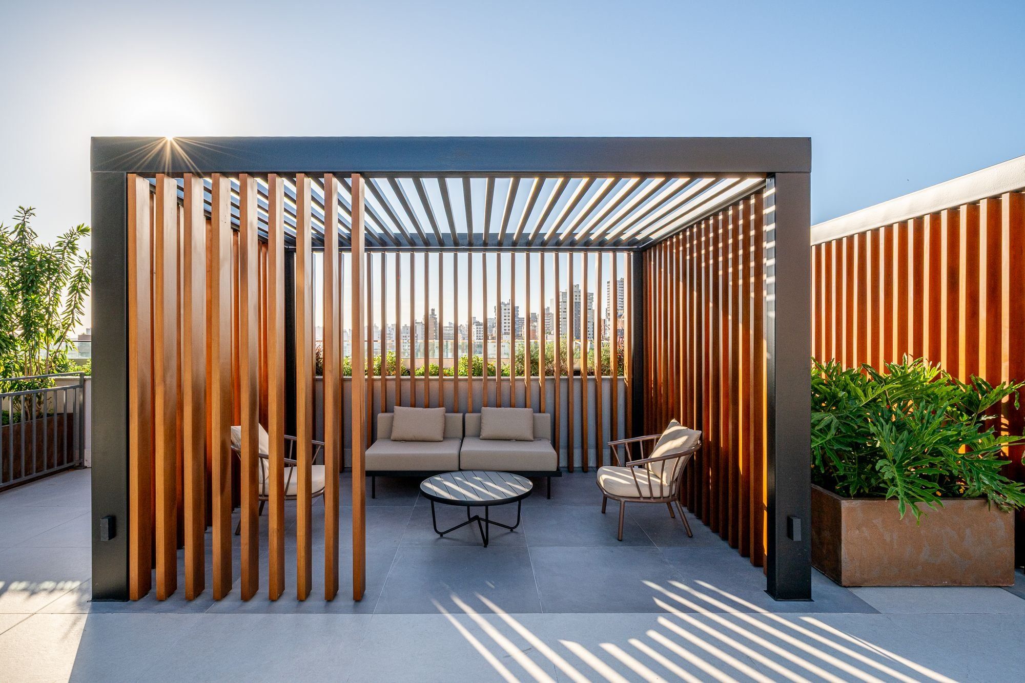 A rooftop patio with a wooden partition, a sofa, two chairs, and a small table.