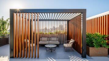 A rooftop patio with a wooden partition, a sofa, two chairs, and a small table.