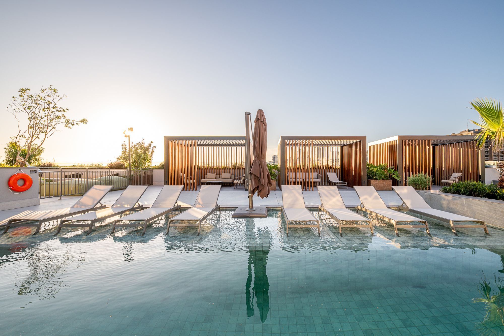 Un área de piscina en la azotea con sillones de descanso, una sombrilla central y paneles de privacidad de madera.