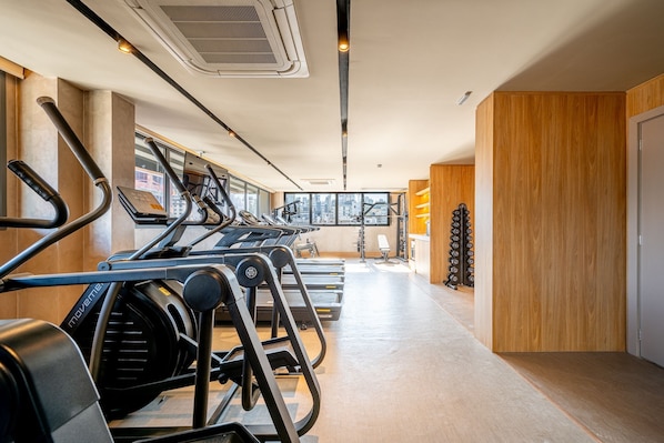Un gimnasio con cintas de correr, bancos de pesas y un amplio ventanal con vistas a la ciudad.