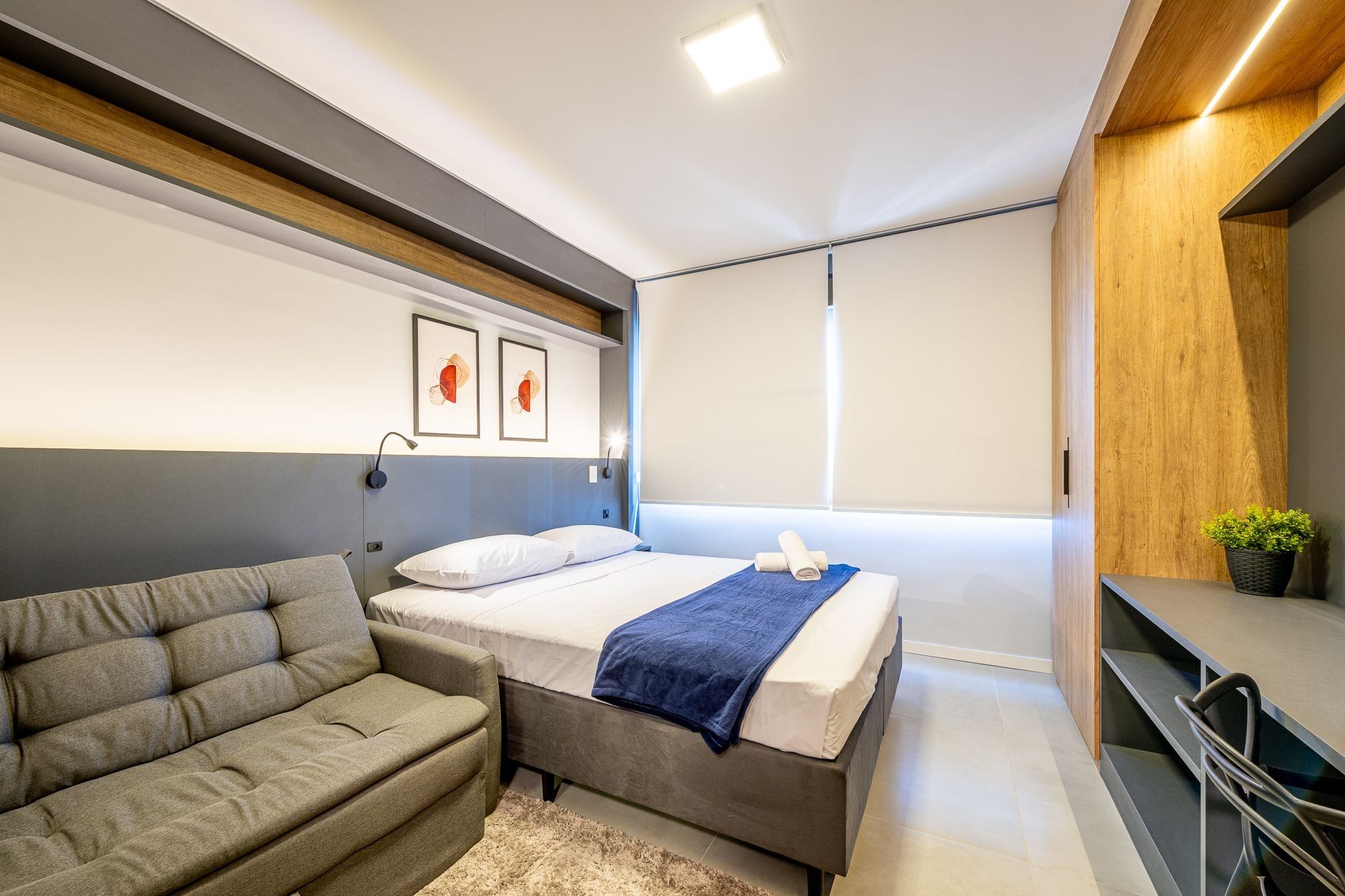 Un dormitorio moderno con cama, sofá, televisión y ventana.