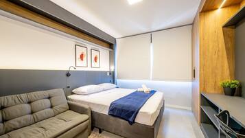 Un dormitorio moderno con cama, sofá, televisión y ventana.
