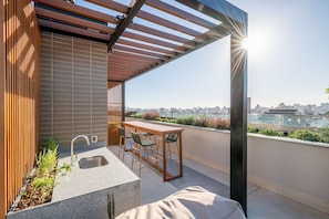 Una terraza en la azotea con una pérgola de madera, un lavamanos empotrado y una mesa con sillas.