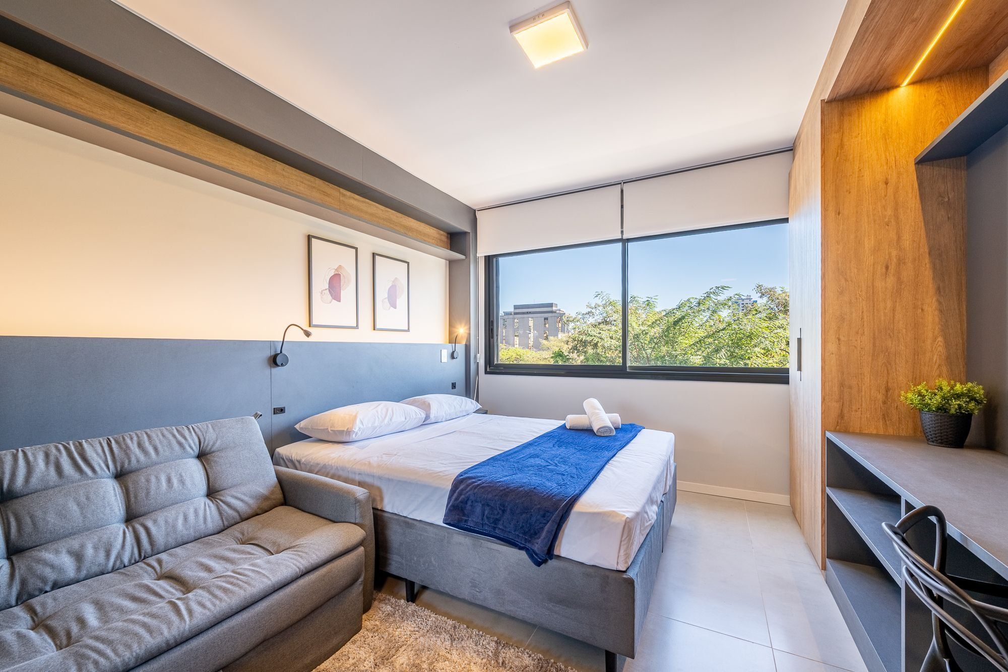 Un dormitorio moderno con cama, sofá, escritorio y un ventanal grande.