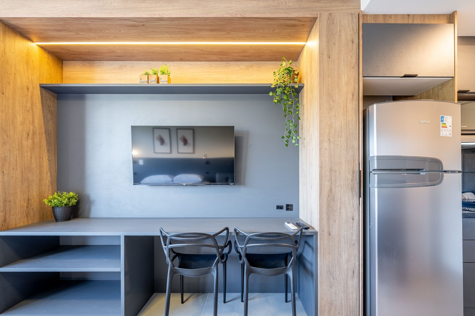 Una cocina moderna con refrigerador empotrado, un televisor de pantalla plana en la pared y dos sillas en una pequeña mesa de comedor.
