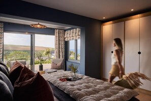 A bedroom with a large bed, a view of the outdoors, and a sliding door closet. - 6 Bed in Mawgan Porth (oc-b584421) (Mawgan Porth)