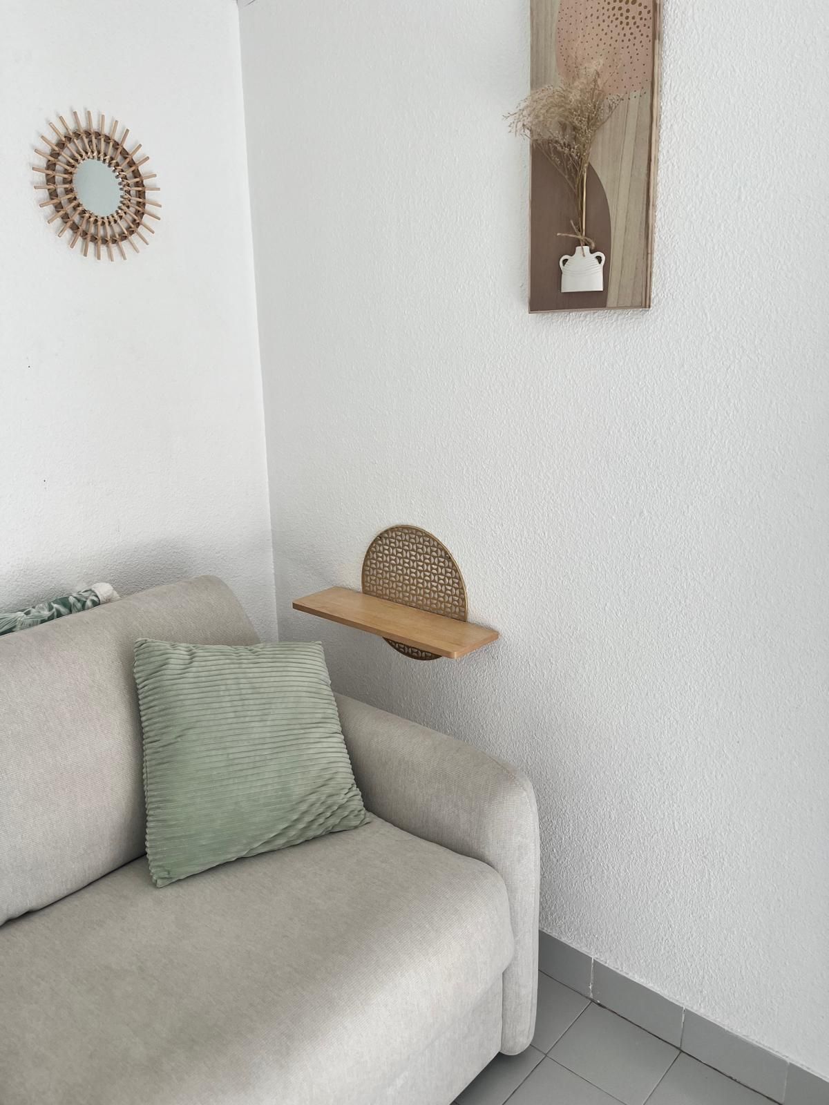 A living room with a sofa, a decorative mirror, a wall-mounted shelf, and a vase with dried plants.