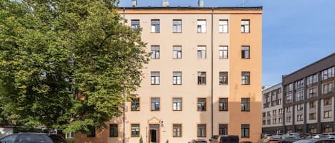 Un immeuble à plusieurs étages doté d’une façade plate, d’un parking à l’avant et d’un grand arbre sur le côté gauche.
