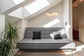 A modern living room with a grey sofa, two black cushions, and a potted plant. - Brand-New Scandi Attic Loft | 5 Separate Beds (Riga)