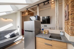 Een kleine keuken met een koelkast, magnetron en een wandgemonteerde flatscreen televisie.