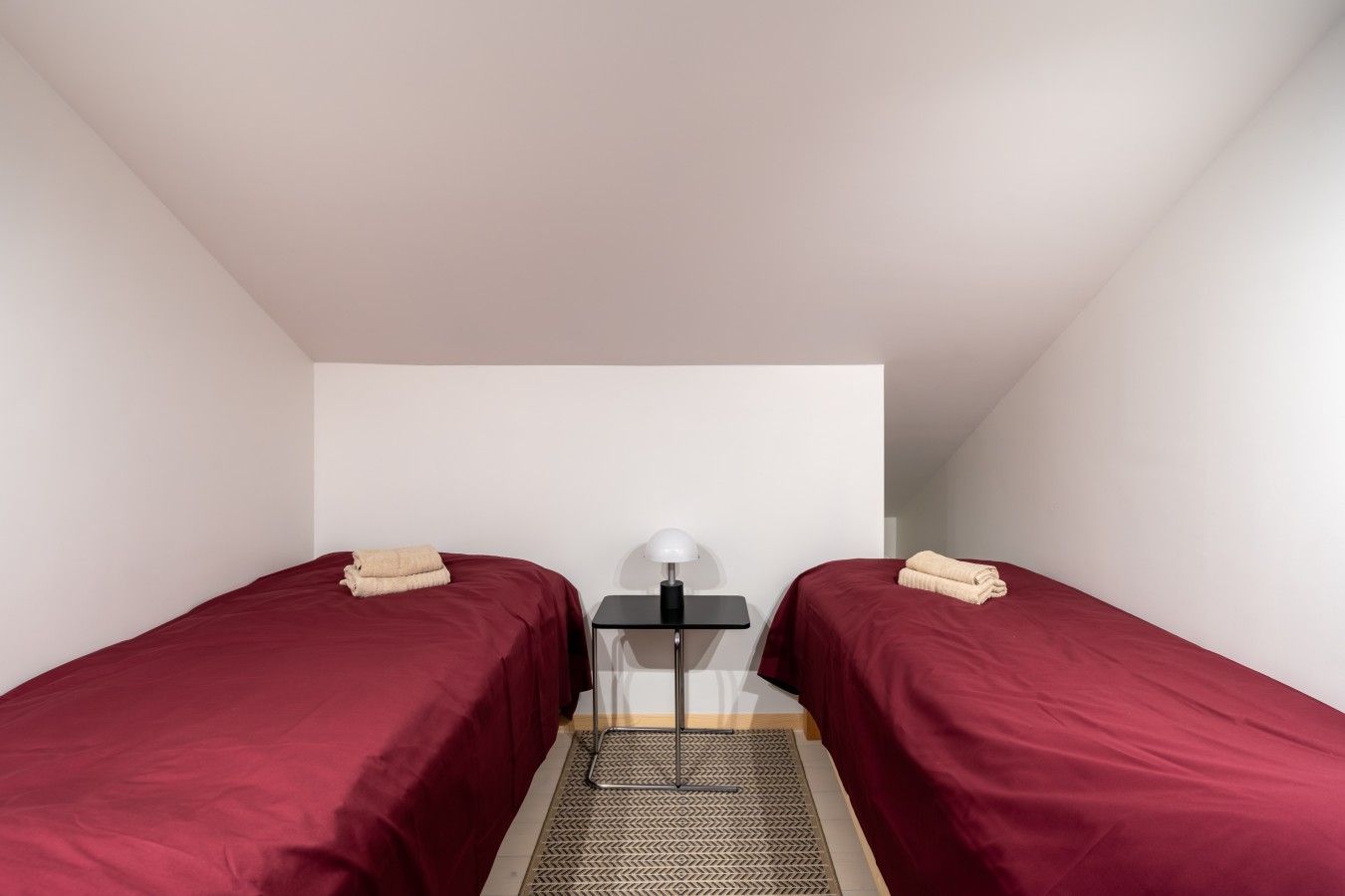 Acomodação compacta, com um quarto e duas camas, mesa de cabeceira com abajur e tapete com padrão no chão.