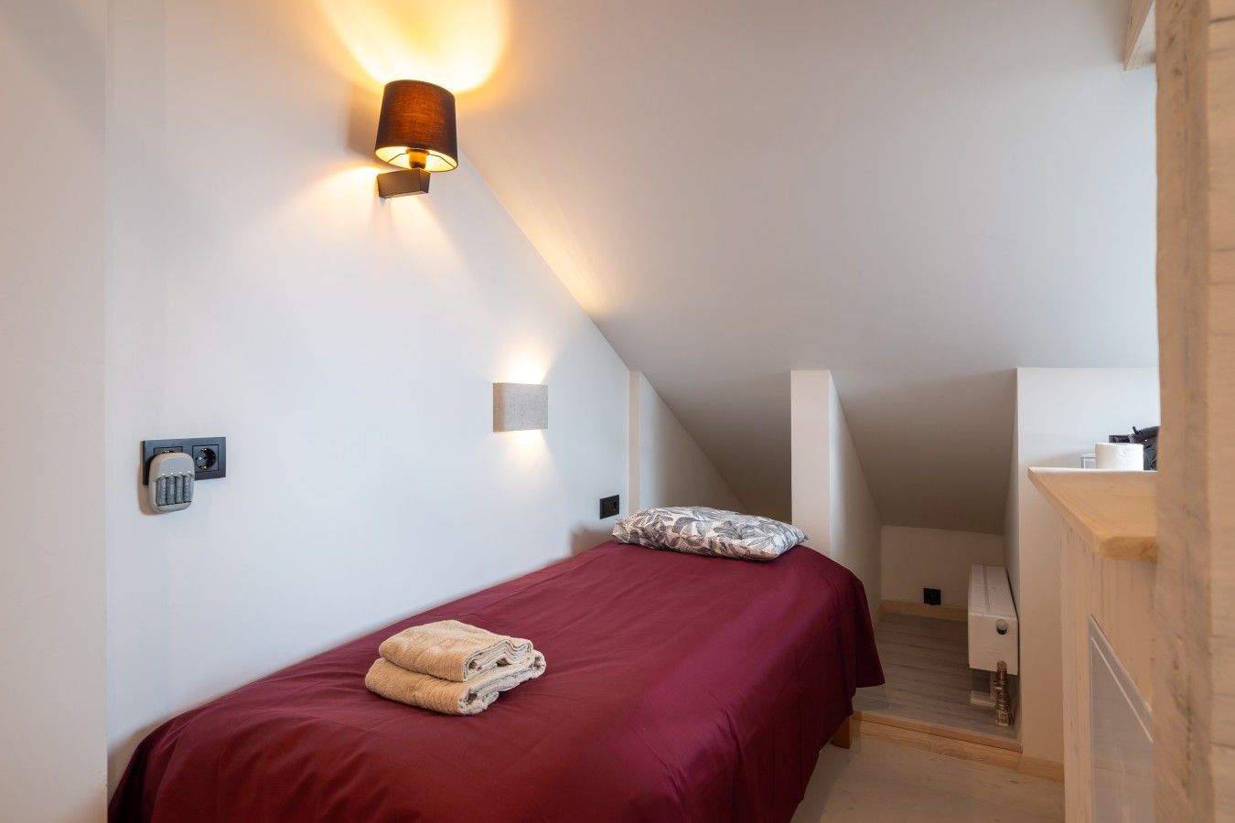 Ein Schlafzimmer mit einem Bett, einer Wandlampe, einem Nachttisch und einem Holzschrank.