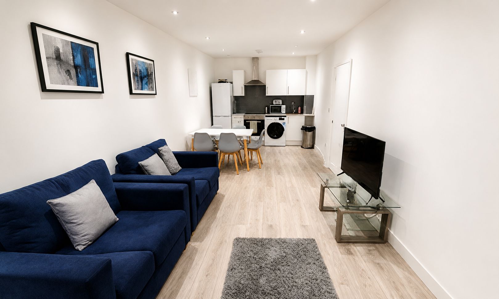 A modern living room with a sofa set, a flat-screen TV, and a dining area with chairs and a table.