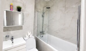 Un baño moderno con ducha envuelta en vidrio, lavamanos blanco y un inodoro.